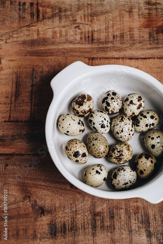 Quail eggs in white ceramic bowl, wood table