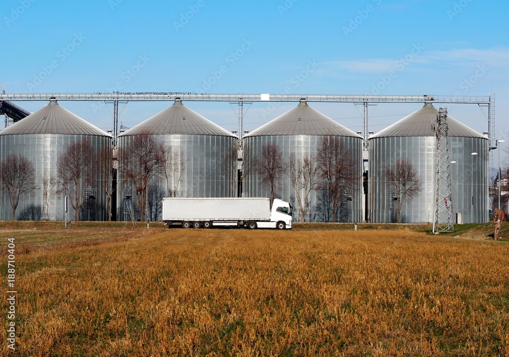White long vehicle trailer truck in front of a grain storage bins White long vehicle trailer truck in front of a grain storage bins