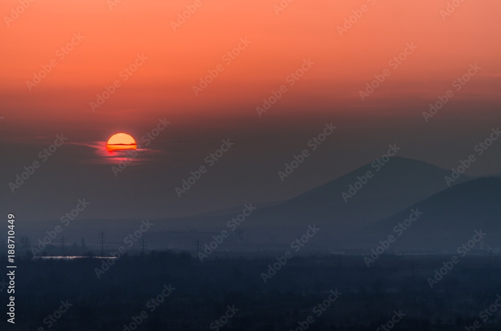 Beautiful sunset landscape with the silhouettes of the hills in the background and sun covered by clouds