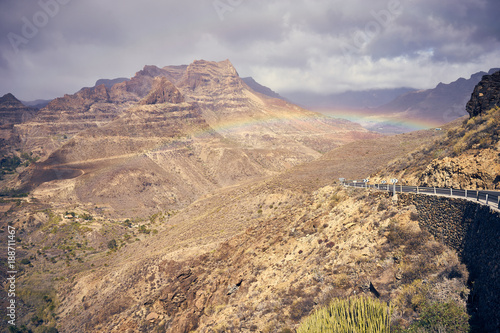 Rainbow over road into mountain landscape of Gran Canaria island, Spain / Valley of "Fataga" seen from the viewpoint "Degollada de la yegua"