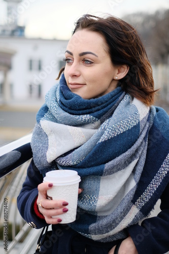 Portrait of attractive young woman wearing scarf and holding white coffee cup on a cold and snowy winter day