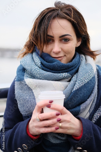 Portrait of attractive young woman wearing scarf and holding white coffee cup on a cold and snowy winter day