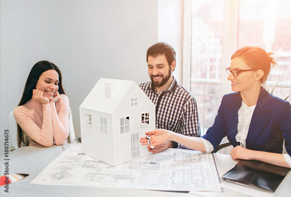 Fototapeta premium Young family couple purchase rent property real estate . Agent giving consultation to man and woman. Signing contract for buying house or flat or apartments. He holds a model of the house in hands