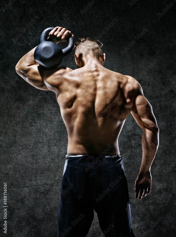 Muscular back of man. Rear view of fitness model with kettlebell on dark background. Strength and motivation