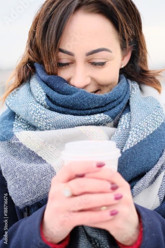 Portrait of attractive young woman wearing scarf and holding white coffee cup on a cold and snowy winter day