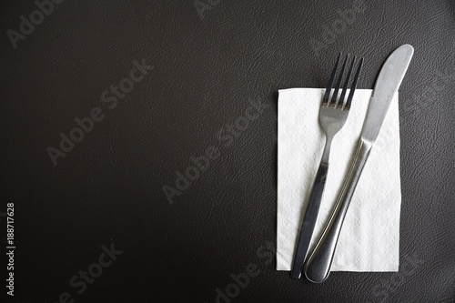 Set of fork and knives with tissue paper on dark brown leather in restaurant.