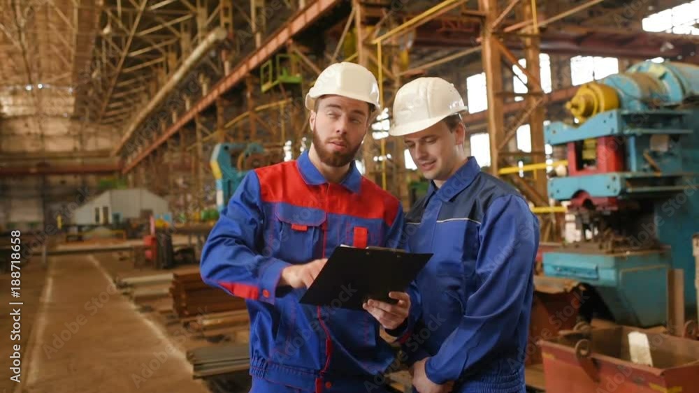 Engineer-constructor and worker discuss the construction project against the background of an industrial plant Engineer-constructor and worker discuss the construction project against the background of an industrial plant