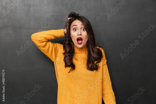 Shocked brunette woman in sweater holding her head