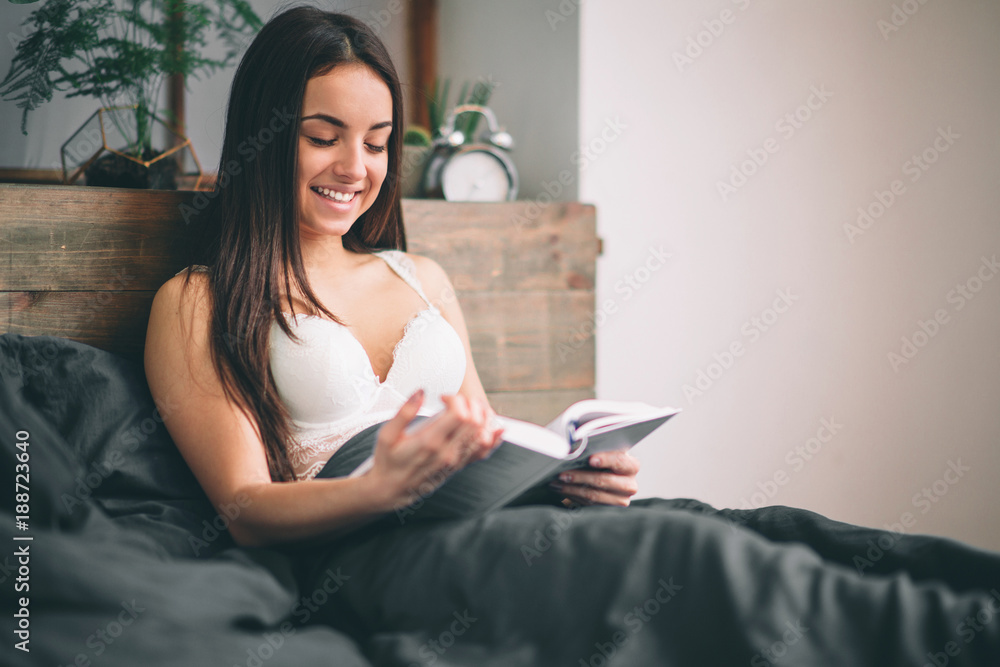 Girl reading book and drinking coffee on the bed. Young woman read a book on black bed linen Girl reading book and drinking coffee on the bed. Young woman read a book on black bed linen