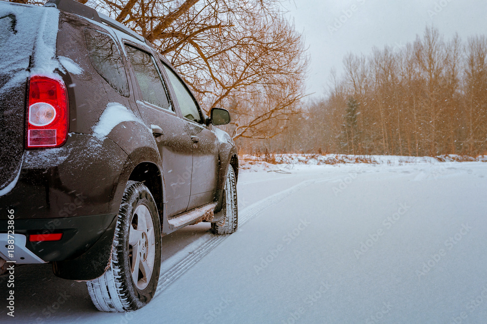 Naklejka premium Dark car on a snowy road on a winter trip close-up of a tire protector, concept of danger on the roads in weather conditions while traveling