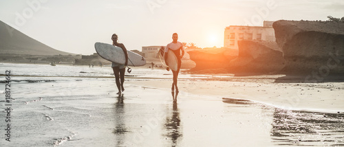 Happy surfers couple running with surf boards on the beach - Sporty people having fun in surfing day - Extreme sport and vacation concept