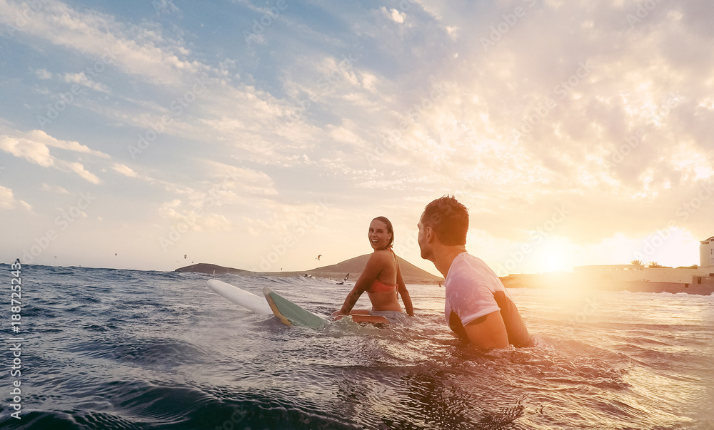 Fit couple surfing at sunset - obrazy, fototapety, plakaty 