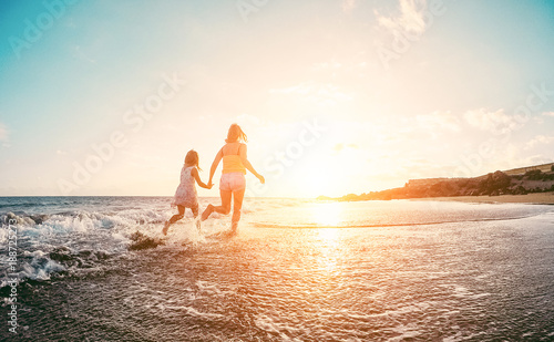 Mother and daughter running inside the water on tropical beach