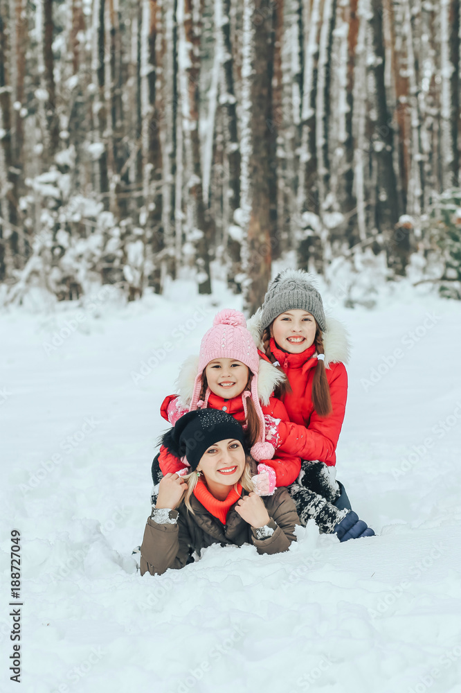 joyful children playing with their mother in the winter forest lying on the snow