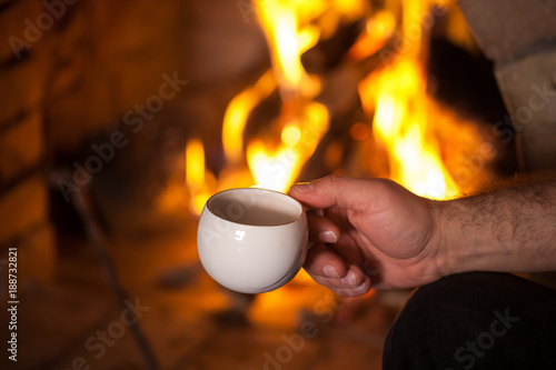 the man's hand with a cup by the fireplace
