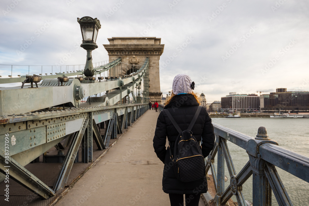 Young woman is standing on the Chain Bridge and looking at the tower on the bridge in Budapest, Hungary.