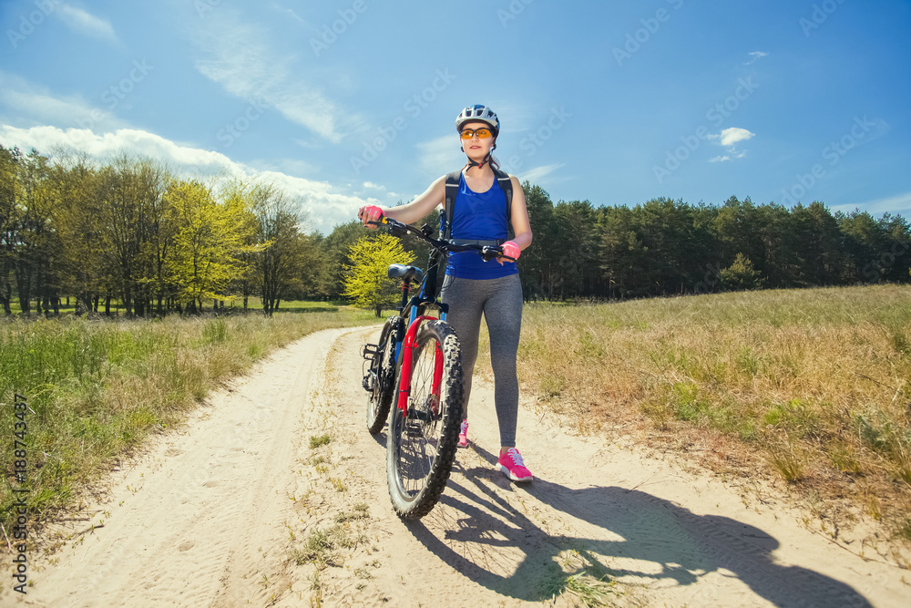 Fototapeta premium One young woman rides on a mountain bike outside of town on the road in the forest on a summer day.