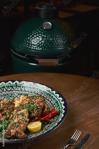 Leg of lamb baked with sauce in a ceramic plate, with garnish from hummus. Grill, oven in the background. selective focus, copy space. photo