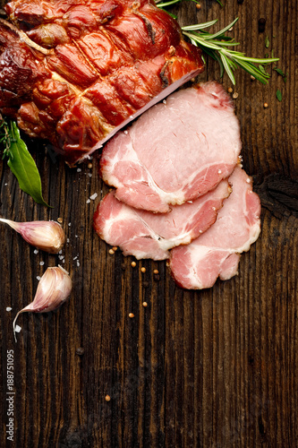  Sliced smoked gammon  on a wooden  table with addition of fresh  herbs and aromatic spices.   Natural product from organic farm, produced by traditional methods