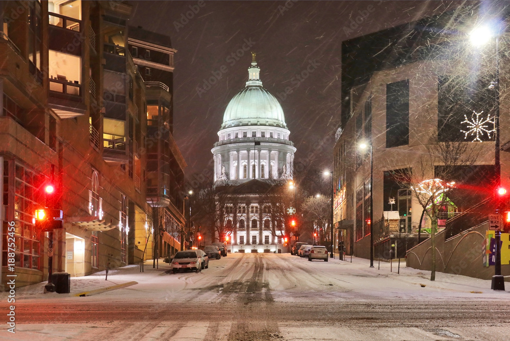 Beautiful night cityscape. Madison, the capitol of Wisconsin downtown street view with parked cars and Wisconsin state capitol building glowing in the snowy night. Wisconsin state, Midwest USA.