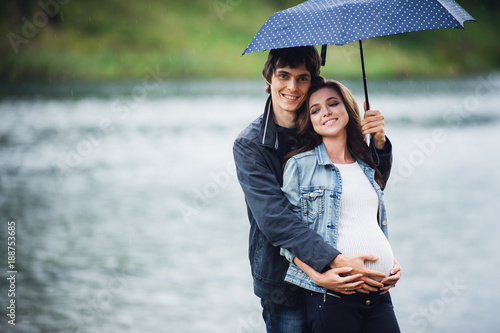 фотографія Pregnant woman and man holding an umbrella at the park in the drizzly day outdoo