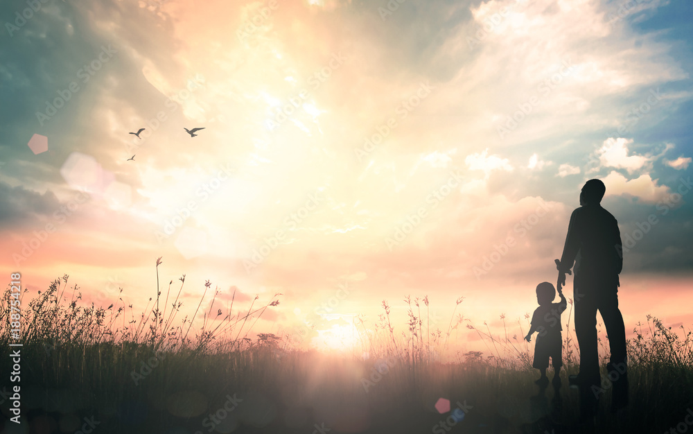 International migrants day concept: Silhouettes father and son holding hand in hand on meadow autumn sunset background