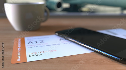 Boarding pass to Basra and smartphone on the table in airport while travelling to Iraq. 3D rendering