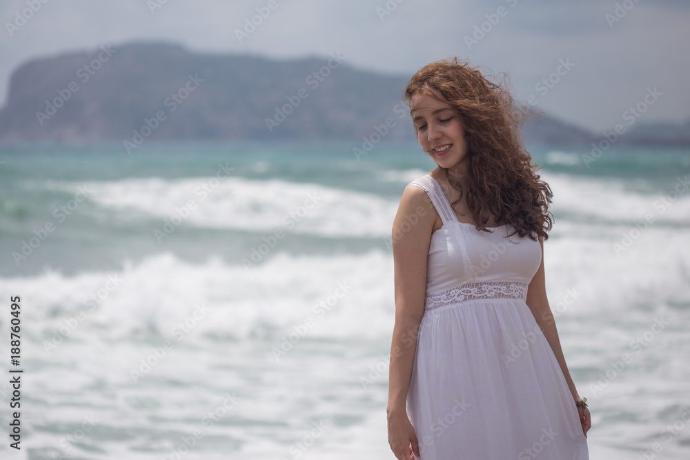 Young brunette female with wavy hair wearing white dress by the