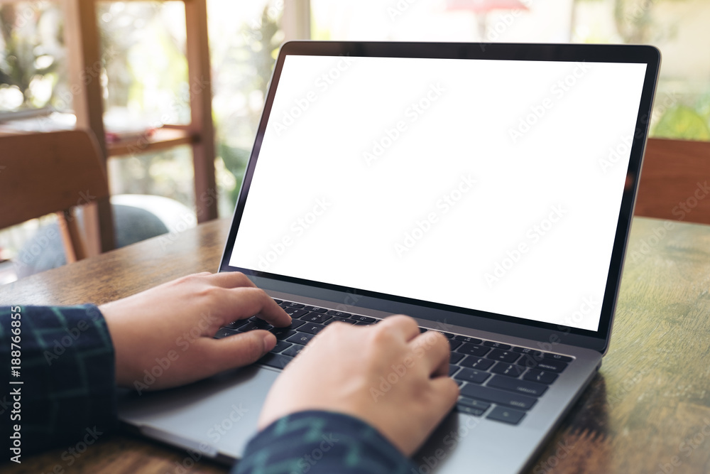 Mockup image of hands using and typing on laptop with blank white desktop screen on wooden table in cafe Mockup image of hands using and typing on laptop with blank white desktop screen on wooden table in cafe