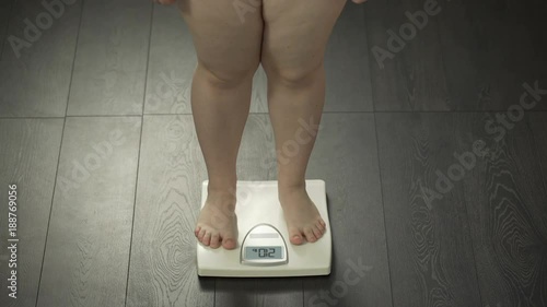 Female with extra weight stepping on bathroom scales, health disorder, obesity