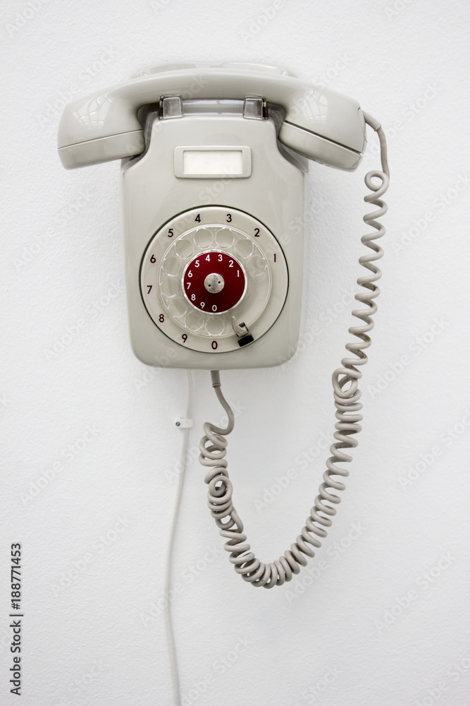 Old fashioned gray rotary telephone hanging on white wall. Vertical photo. Old fashioned gray rotary telephone hanging on white wall. Vertical photo.