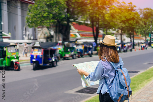 Young woman traveler with sky blue backpack and hat looking map find the way with tuk tuk thailand background from wat pho at Bangkok Thailand