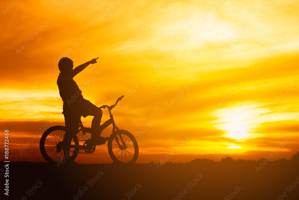 Fototapeta premium silhouette boy riding bicycle at sunset or sunrise background