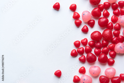 Scattered Valentine's Day cinnamon heart candies with red and pink jelly beans on white background