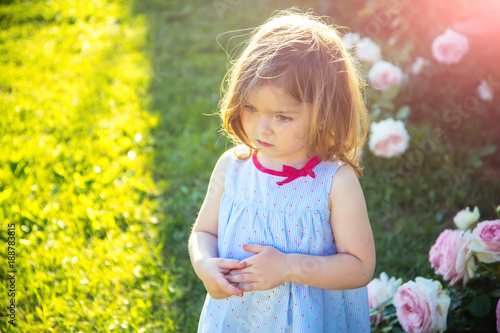 Child with thinking face in blue dress at blossoming roses