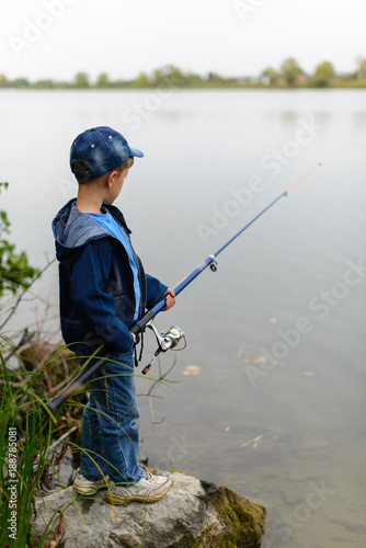A fisherman boy on the river bank with a fishing rod in his hands. He wants to catch a big fish..