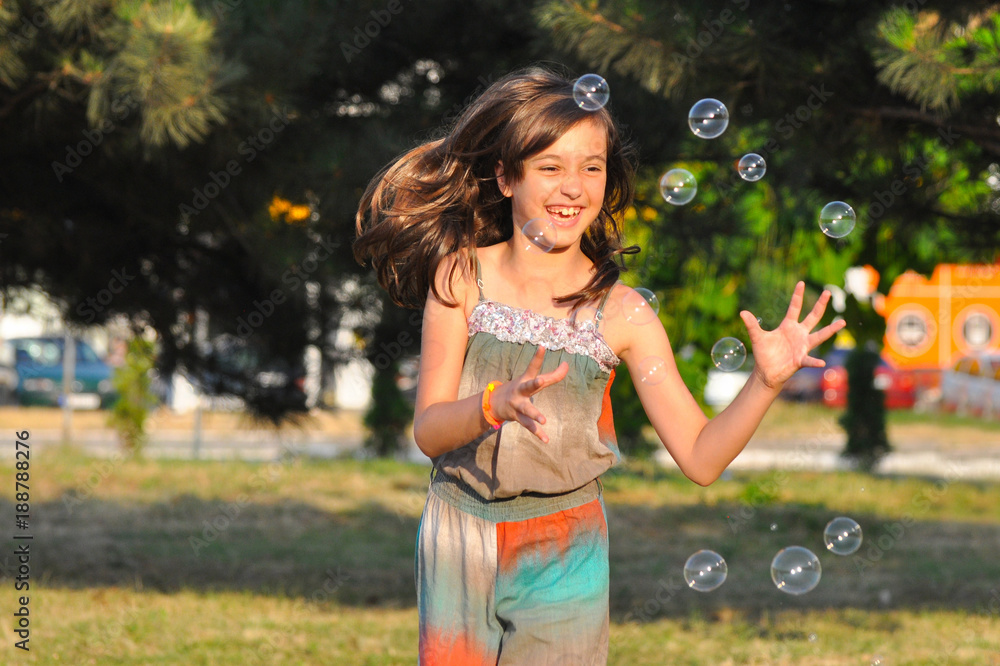 Happy smiling girl catching soap bubbles in summer park. Little girl play in the park with soap bubbles Happy smiling girl catching soap bubbles in summer park. Little girl play in the park with soap bubbles