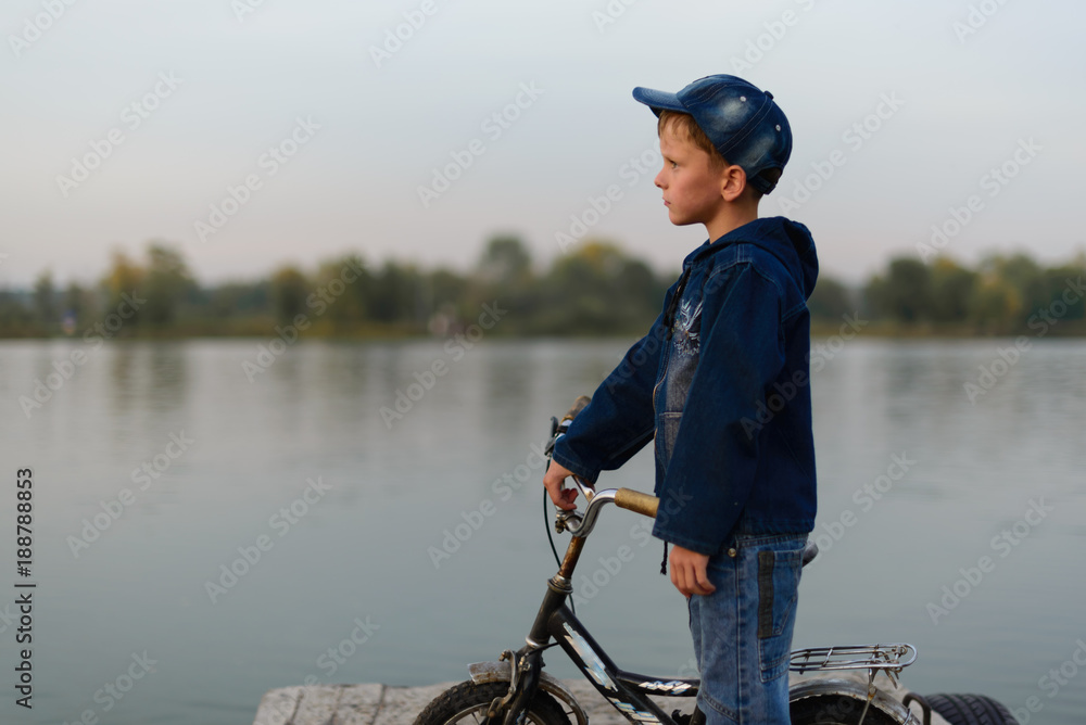 The boy on the river bank is traveling. He came by bicycle. He looks at the watery surface.. The boy on the river bank is traveling. He came by bicycle. He looks at the watery surface..