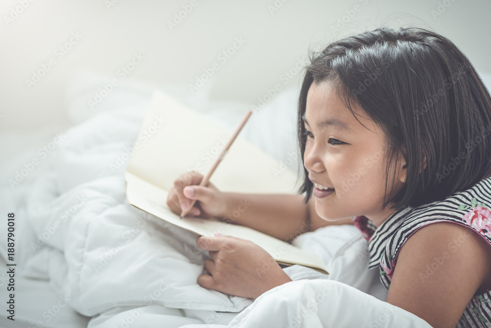 Cute Asian girl writing the book while lying on the bed,Learning and education concept Cute Asian girl writing the book while lying on the bed,Learning and education concept
