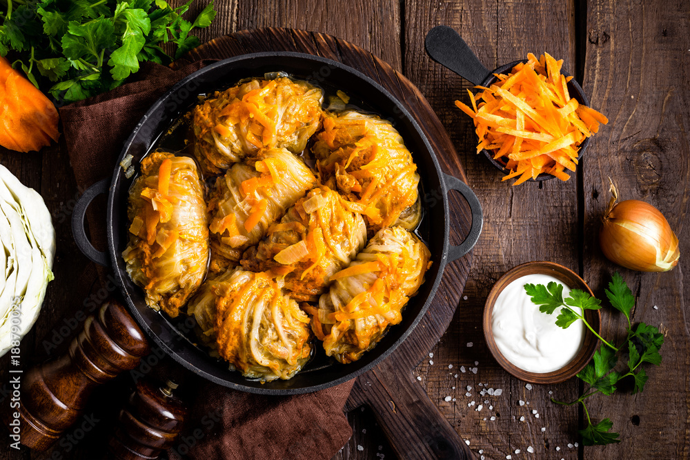 Cabbage rolls stewed with meat and vegetables in pan on dark wooden background, top view