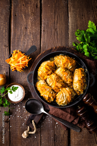 Cabbage rolls stewed with meat and vegetables in pan on dark wooden background, top view