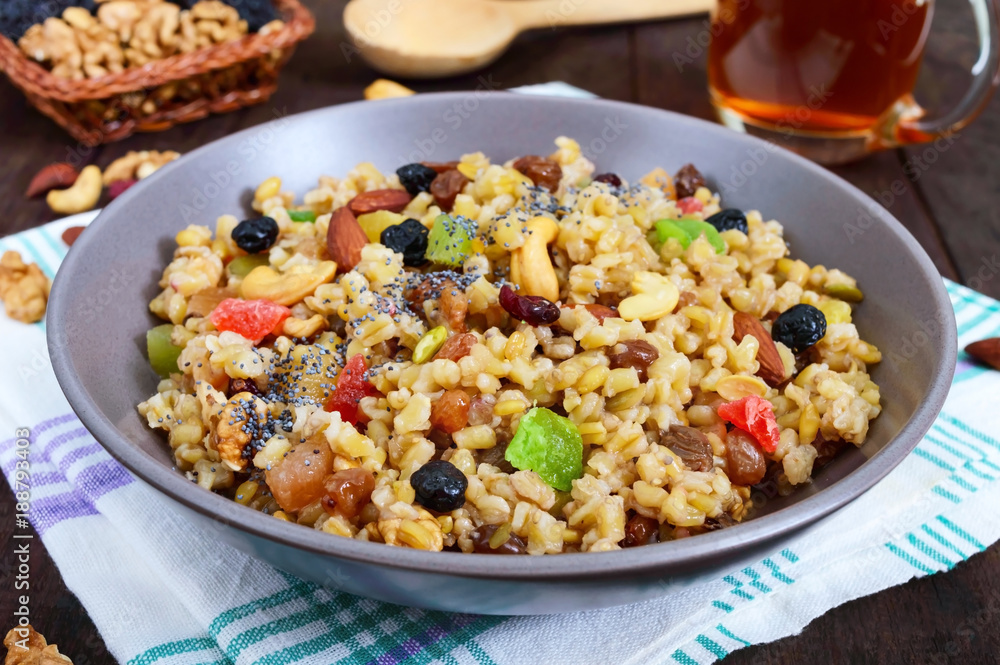 Wheat porridge with nuts, dried berries, raisins, poppies in a ceramic bowl on a dark wooden background. Proper nutrition. Healthy food. Wheat porridge with nuts, dried berries, raisins, poppies in a ceramic bowl on a dark wooden background. Proper nutrition. Healthy food.