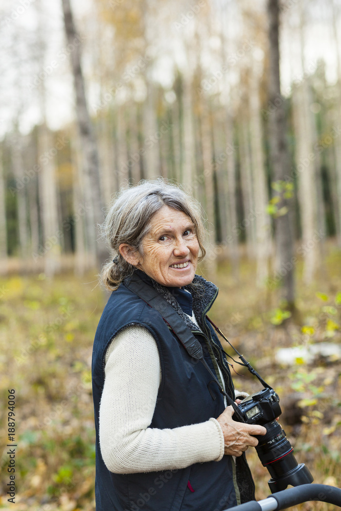 Smiling senior woman with camera in forest