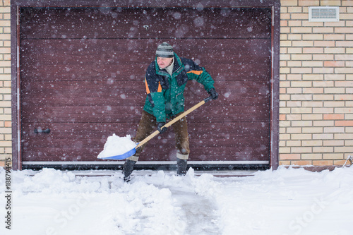 Картината върху платно A man cleans snow in winter weather with a shovel near the garage