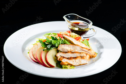 Roasted juicy pork steak with apples and soy sauce in a white plate isolated on black background
