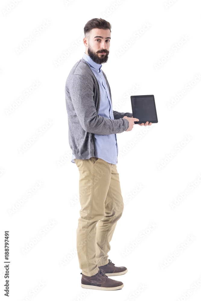 Side view of young bearded business man showing and pointing at blank tablet screen. Full body length portrait isolated on white studio background. Side view of young bearded business man showing and pointing at blank tablet screen. Full body length portrait isolated on white studio background.