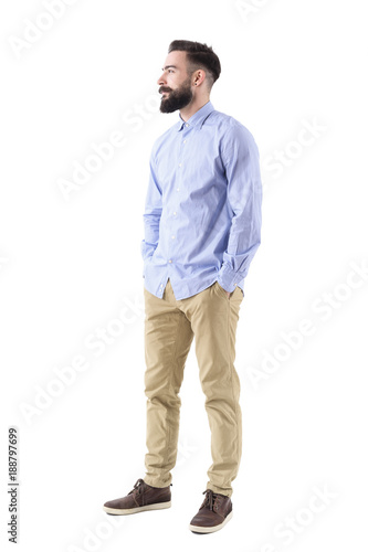 Side view of elegant handsome bearded business man looking up smiling with hands in pockets. Full body length portrait isolated on white background. 