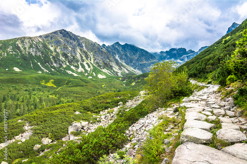 Hiking trail in mountains, panoramic landscape of path over valley with green forest, evergreen nature in wilderness