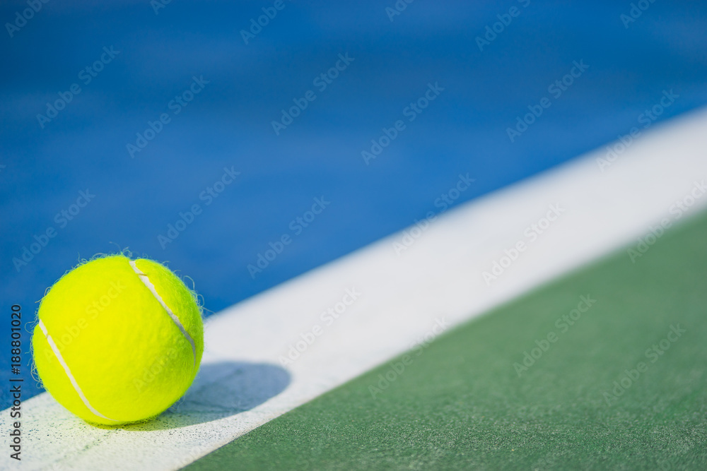 one new tennis ball on white diagonal line in blue and green hard court with light from left, shadow and copy space on right