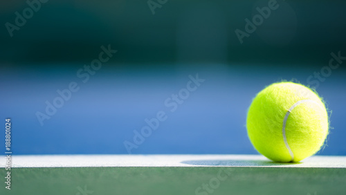 one new tennis ball on white line in blue and green hard court with light from right, shadow and copy space on left